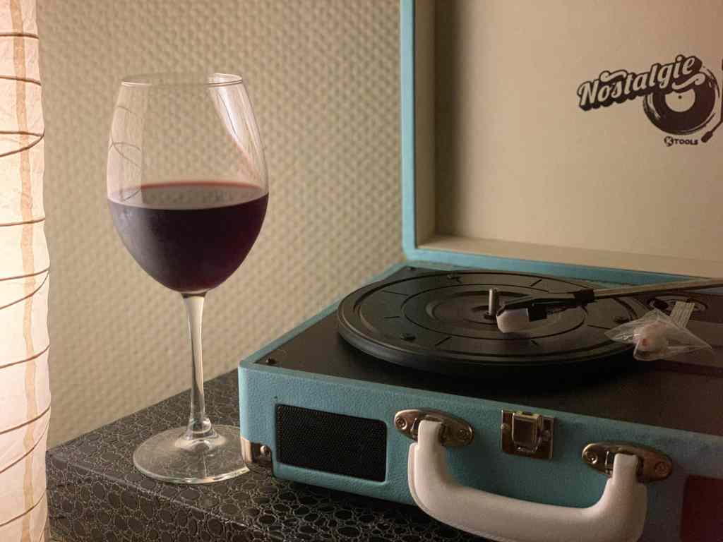A glass of red wine beside a vintage turntable evokes nostalgia and elegance.