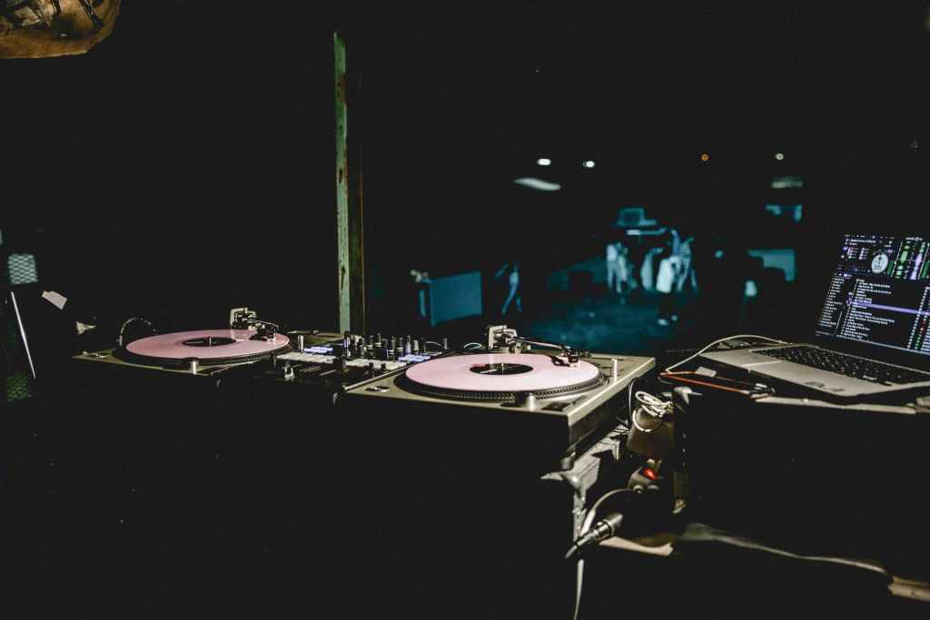 Platos de DJ, mesa de mezclas y ordenador portátil en el ambiente de un club a oscuras, captando el ambiente de la vida nocturna.