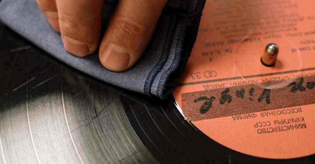 A hand gently wipes a vintage vinyl record on a turntable with a soft cloth, preserving its analog charm.