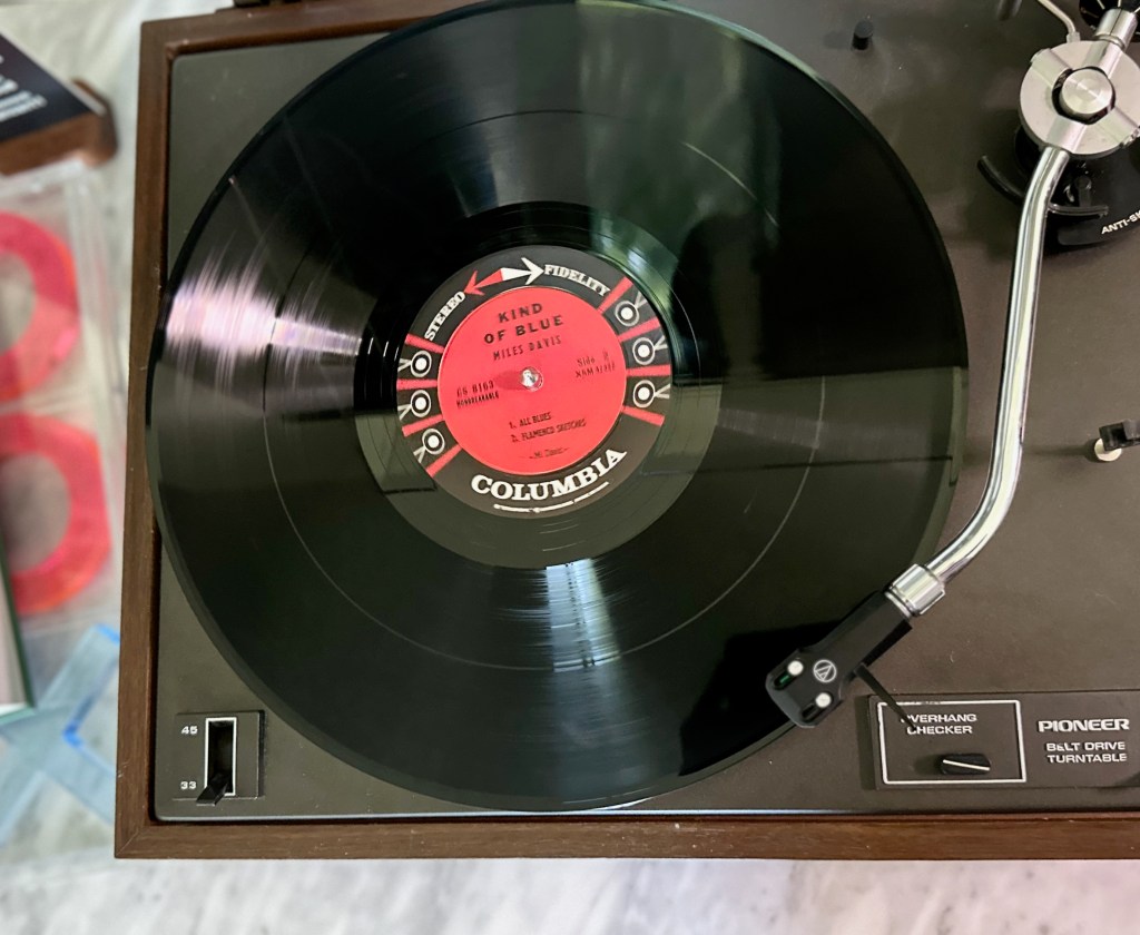 Original Columbia six-eye stereo pressing of Miles Davis’ Kind of Blue spinning on a Pioneer PL-12D turntable with visible red Columbia label and vintage woodgrain plinth.