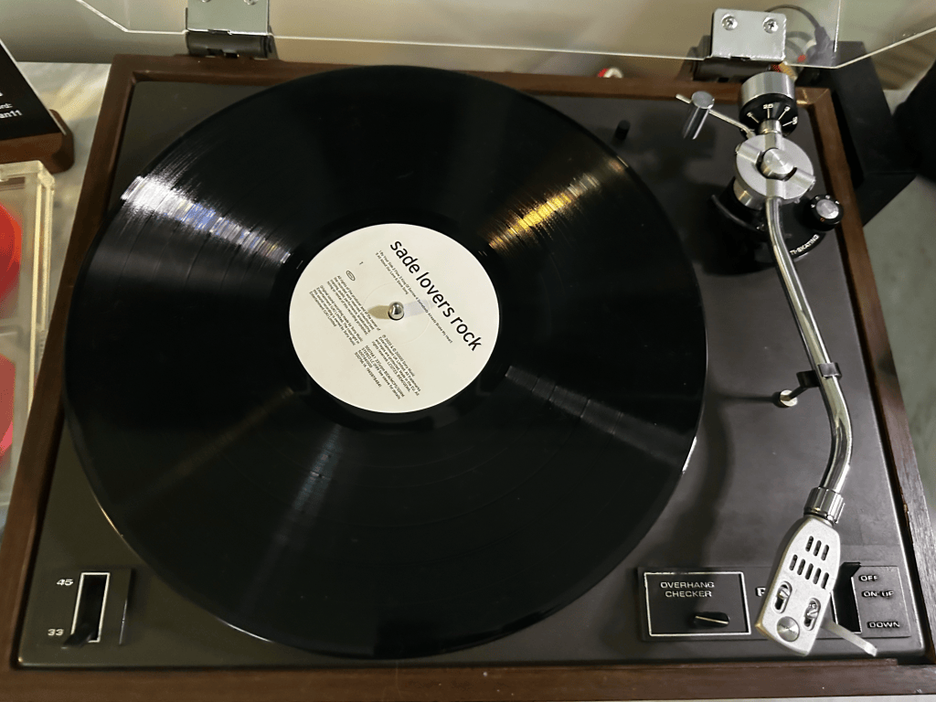 Sade Lovers Rock vinyl on a wood-trimmed turntable with the dust cover raised and tonearm resting beside the record.